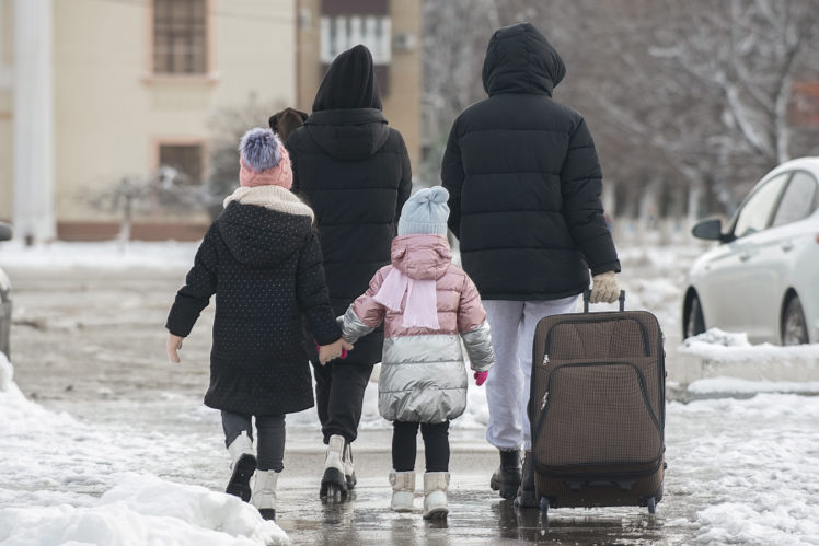 Une famille de 4 personnes marche de dos dans la neige avec des bagages