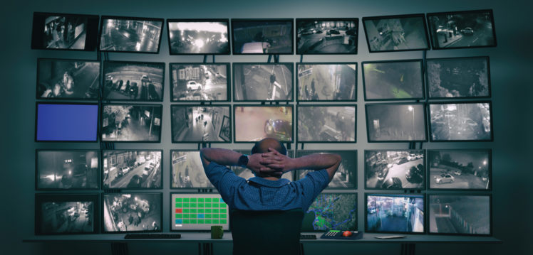 Un homme de dos face à un mur d’écran de videosurveillance